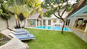 A pool area with lounge chairs, a small pool, and a thatched-roof structure.