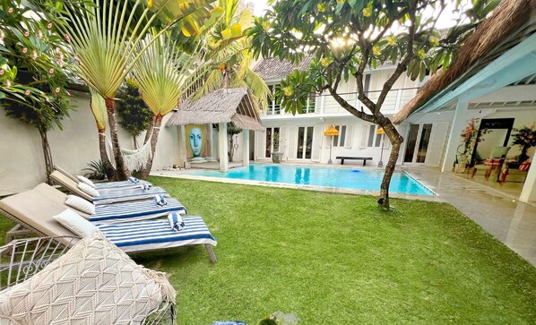 A pool area with lounge chairs, a small pool, and a thatched-roof structure.