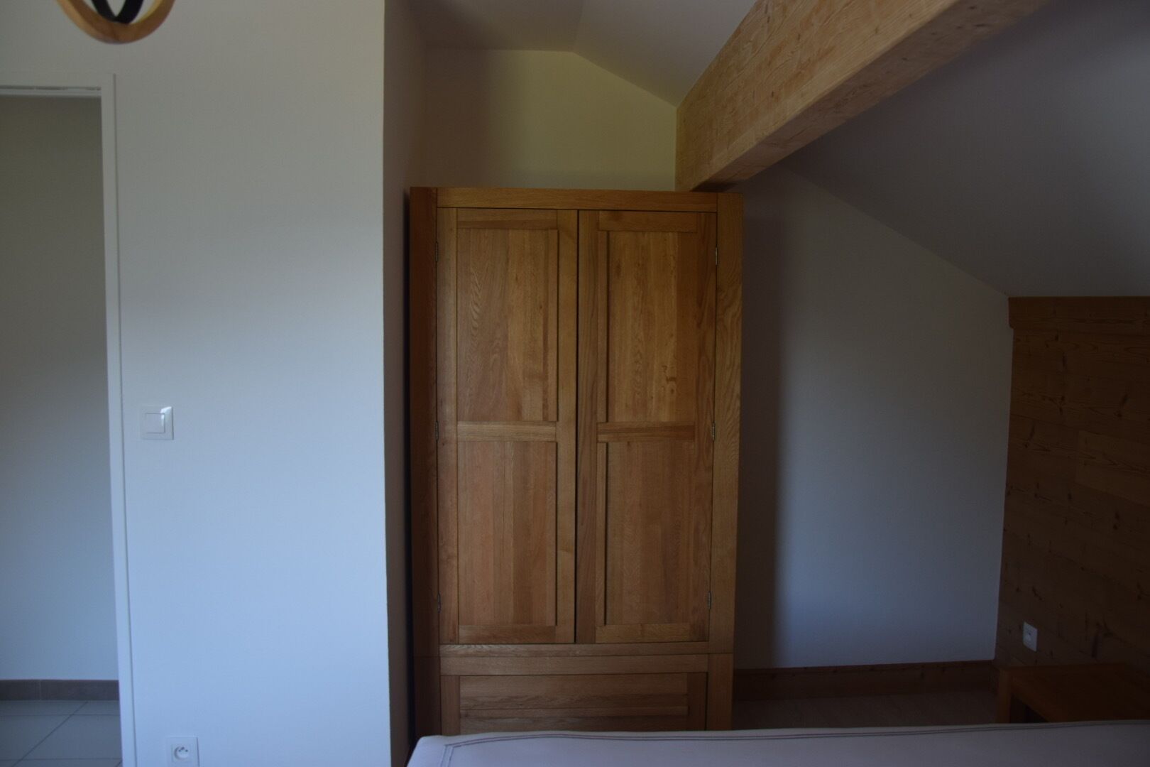 A room with a wooden wardrobe, a white door, and a sloped ceiling.