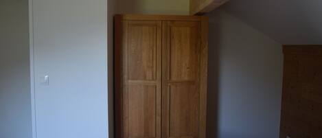 A room with a wooden wardrobe, a white door, and a sloped ceiling.