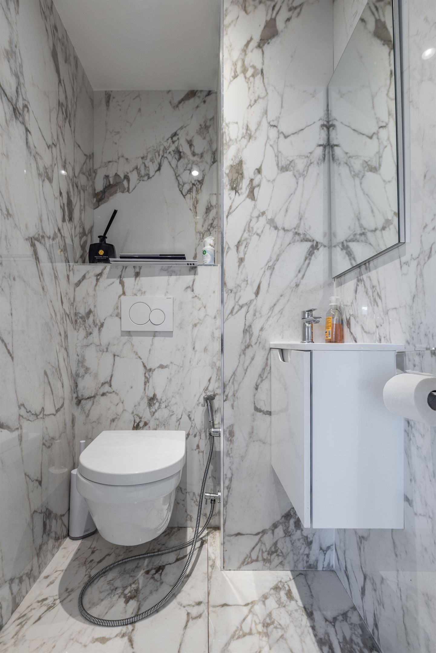 Une salle de bain moderne avec un sol et des murs en marbre, des toilettes blanches, une douche en verre et un meuble-lavabo avec un miroir.