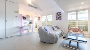 A modern living room with a sofa, a glass coffee table, and a dining area with a white table and chairs.