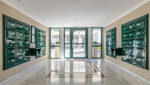 A lobby with green mailboxes, a marble floor, and a view of the street through glass doors.