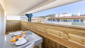 A balcony with wooden railings, a table with breakfast items, and a view of buildings in the background.