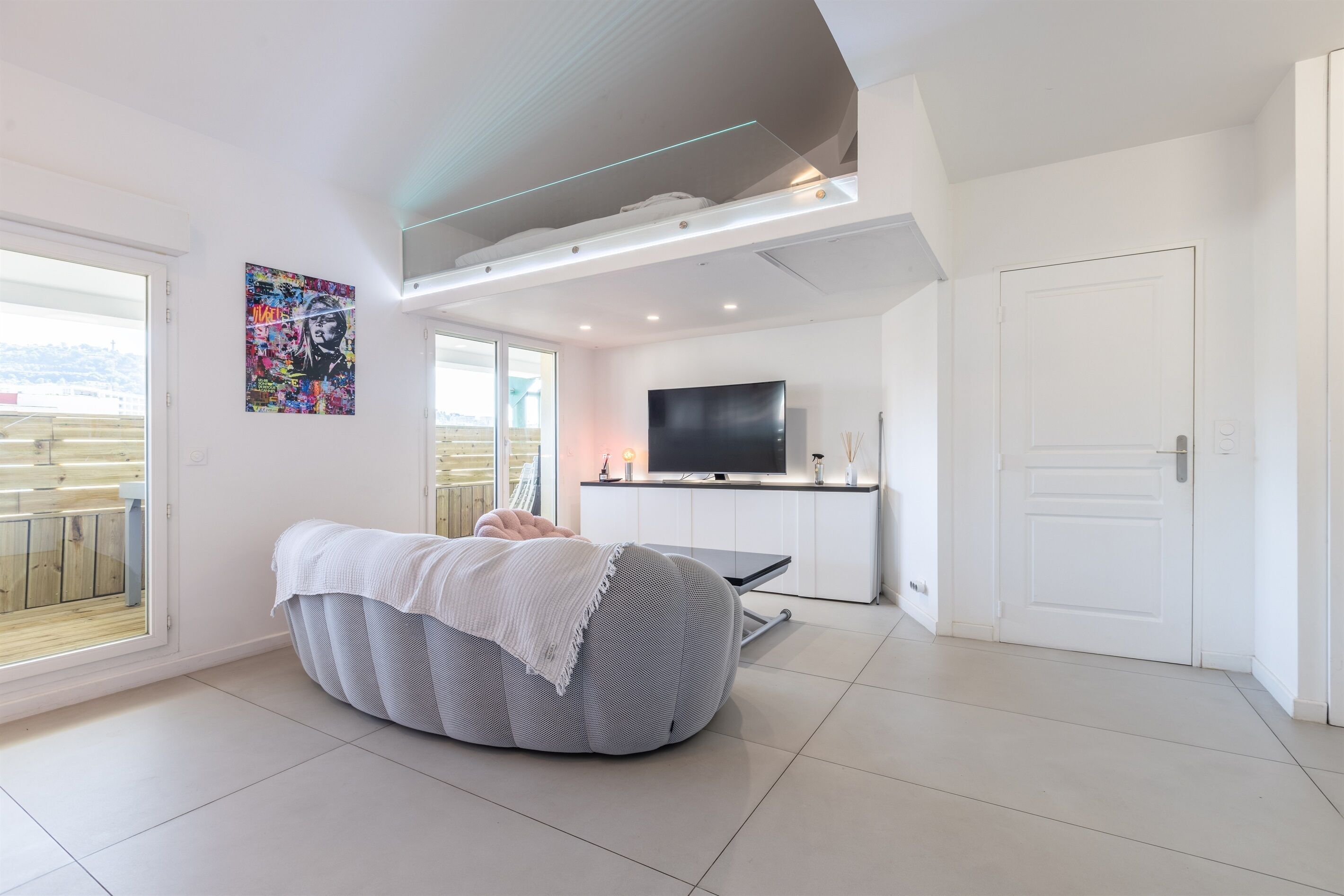 A modern living room with a large bean bag, a flat-screen TV, and a kitchen area.