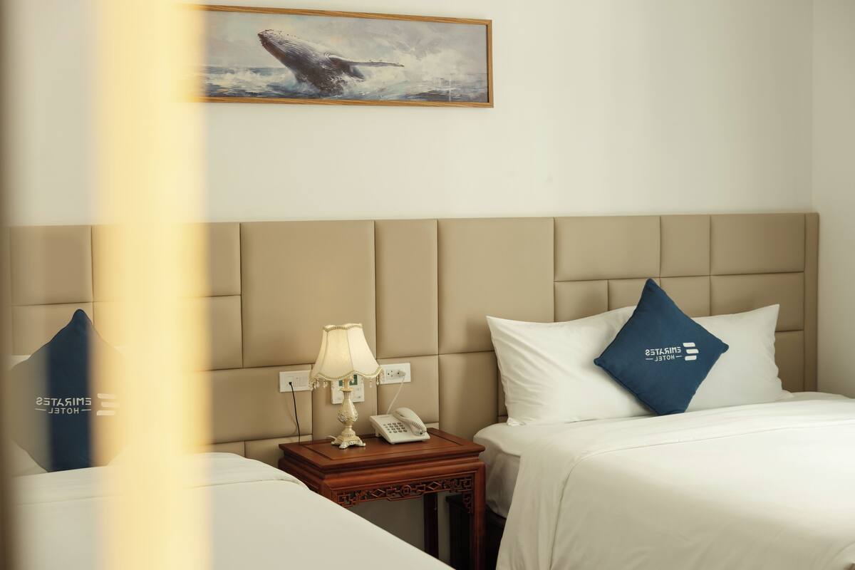 A hotel room with a bed, a nightstand with a lamp and phone, and a painting on the wall.