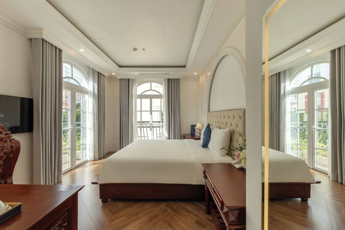 A spacious bedroom with a large bed, a wooden desk, and a television.