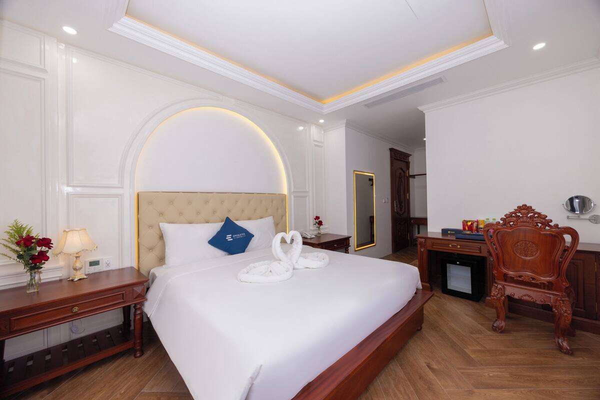 A hotel room with a large bed, a wooden nightstand, a desk, a mirror, and a chair.
