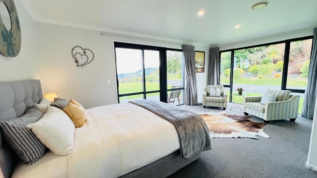 Un dormitorio con una cama grande, vistas al exterior a través de una puerta corredera y una zona de estar con dos sillones.