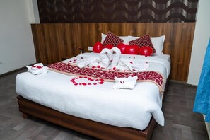 Een netjes opgemaakt bed met een houten hoofdeinde, witte beddengoed en hartvormige rode kussens.