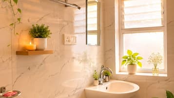 A bathroom with a toilet, sink, shower, towel rack, and plants.