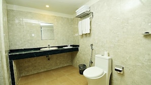 Une salle de bain avec un sol en marbre, des toilettes blanches, un lavabo avec un plan de toilette noir et un porte-serviettes avec des serviettes pliées.