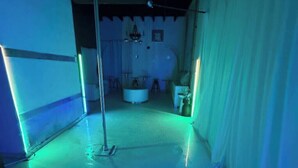 Una habitación con piso blanco, un poste, una cortina blanca y una mesa redonda con sillas.