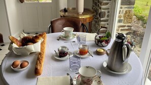Une table de salle à manger ronde, recouverte d’une nappe blanche, mise avec du pain, des œufs, une théière, des tasses et un vase rempli de fleurs.