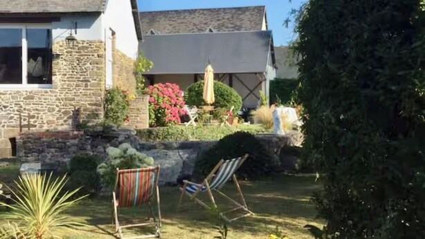 Un bâtiment en pierre avec un toit en pente, un jardin avec une pelouse et un petit espace piscine.