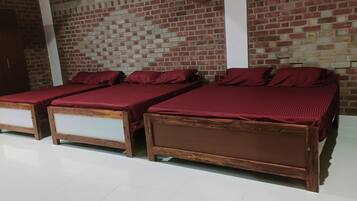 Tres camas de madera con ropa de cama roja en una habitación con paredes de ladrillo y suelo blanco.