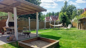 Een achtertuin met een houten pergola, een barbecue, een vuurkorf en een hangmat.