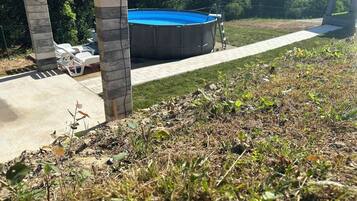 A backyard with a swimming pool, a covered patio area, and a grassy lawn.