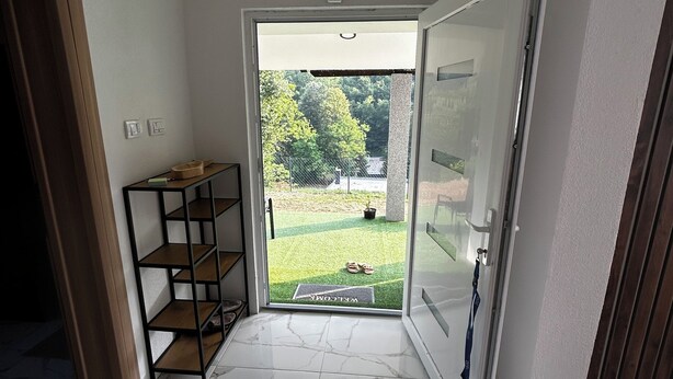 Habitación con piso de mármol, repisa de madera y puerta que da a un espacio exterior verde con felpudo.