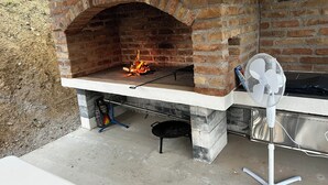 Zona de barbacoa al aire libre con horno de ladrillo, un ventilador y utensilios para asar.