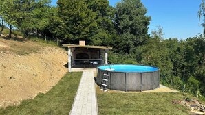 Un patio trasero con zona de barbacoa de ladrillo, piscina y un sendero pavimentado.