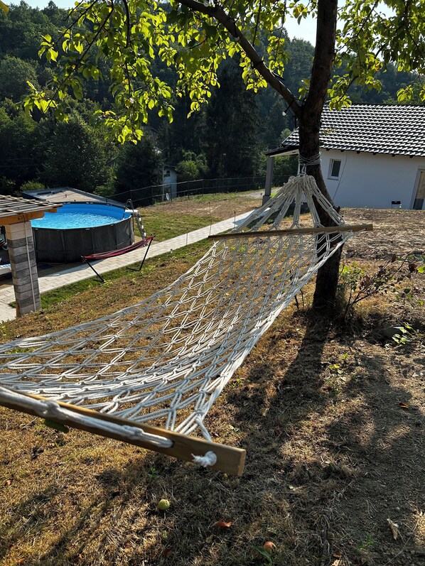 A hammock under a tree, a swimming pool, and a house in the background.