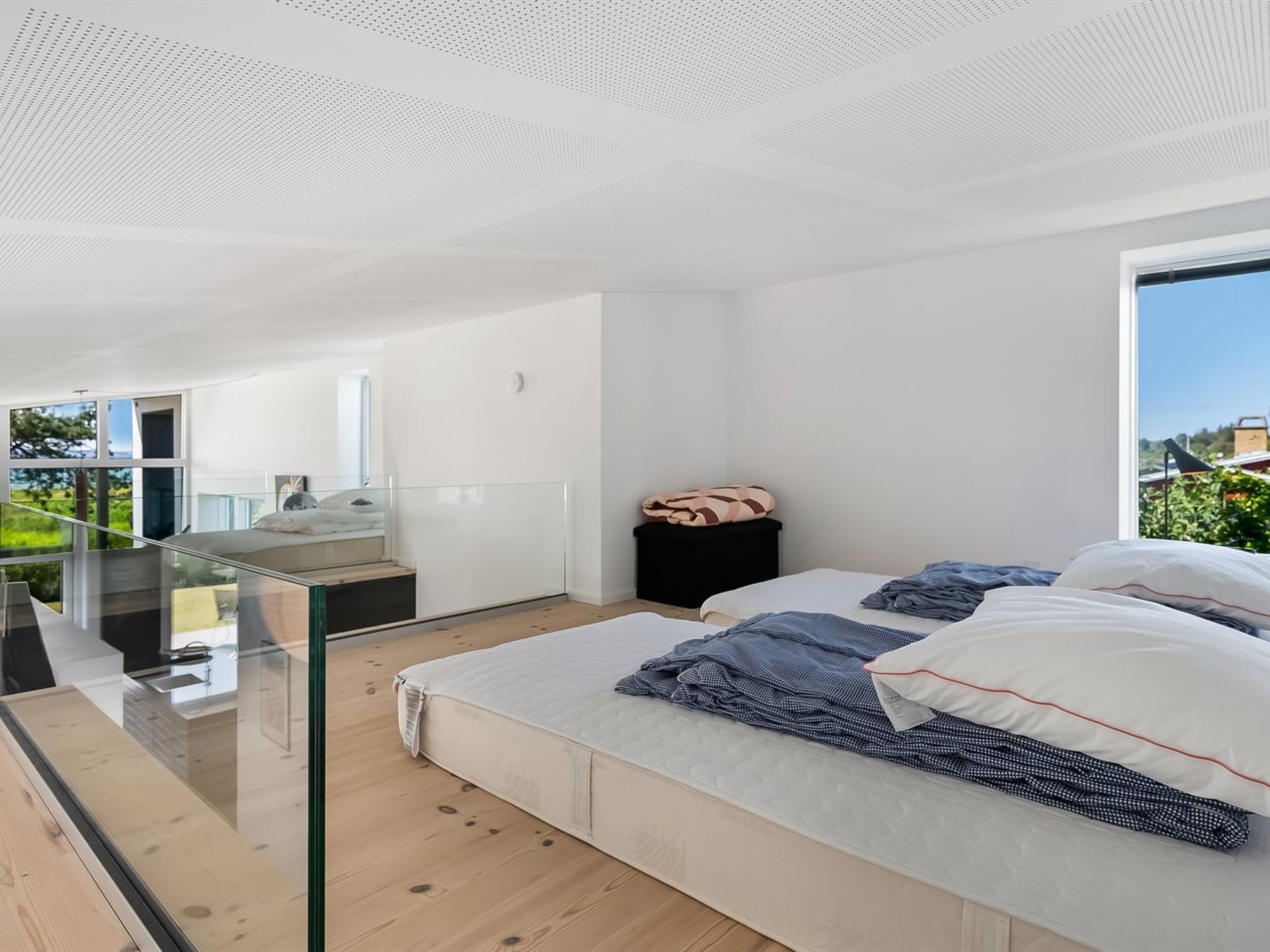 Een moderne slaapkamer met een glazen balkon, een bed met kussens en een klein zwart krukje.