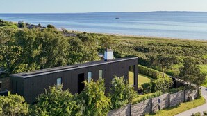 Ein modernes Gebäude mit flachem Dach, umgeben von üppigem Grün und Blick auf das Meer.