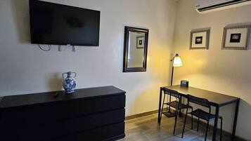 Une pièce dotée d’un téléviseur à écran plat fixé au mur, d’une petite table avec deux chaises, d’une lampe et d’un vase décoratif posé sur une commode.