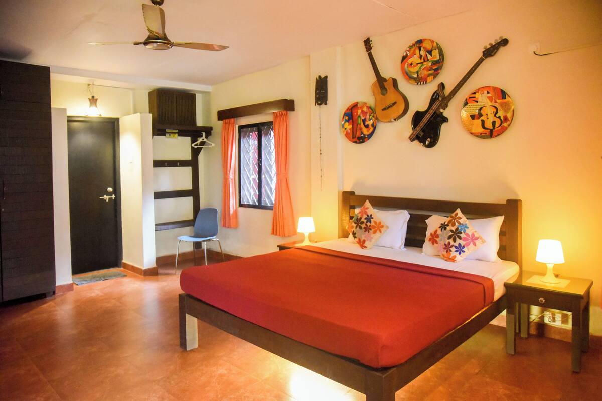 A hotel room with a bed, a chair, a desk, and a guitar wall art.