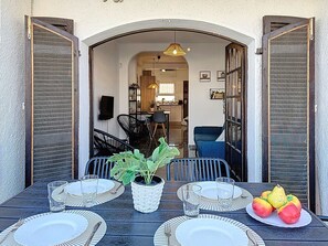 Un espace extérieur aménagé pour les repas, avec une table dressée pour quatre personnes, une plante en pot et une assiette de fruits.