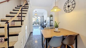 Eine Treppe mit Seilgeländer, ein Essbereich mit Holztisch und Stühlen, ein Blumentopf und eine Wanduhr.