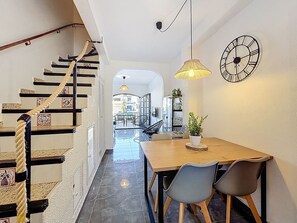 Un escalier avec une rampe en corde, un coin repas avec une table et des chaises en bois, une plante en pot et une horloge murale.