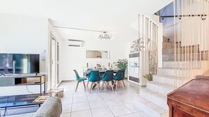 Una sala de estar moderna con televisor, sofá y comedor con sillas y mesa.