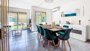 Un comedor con una mesa grande, sillas y una araña. Hay un televisor sobre un mueble bajo y una encimera blanca con un espejo encima.
