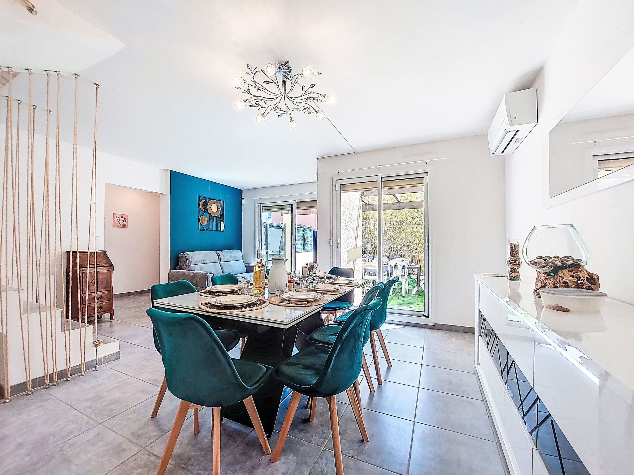 Een moderne eetruimte met een grote tafel, blauwgroene stoelen en een bijzondere kroonluchter.