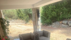 A covered patio area with a stone wall, a cushioned seating arrangement, and a view of a natural landscape. - Guest room 21m2 (Figari)