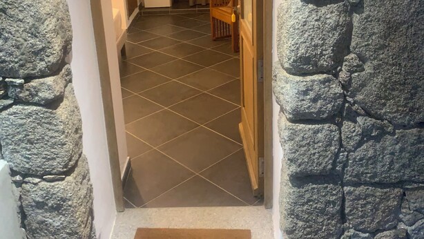 A stone-walled hallway leading to a room with a tiled floor, a wooden chair, and a door with a handle. - Guest room 21m2 (Figari)