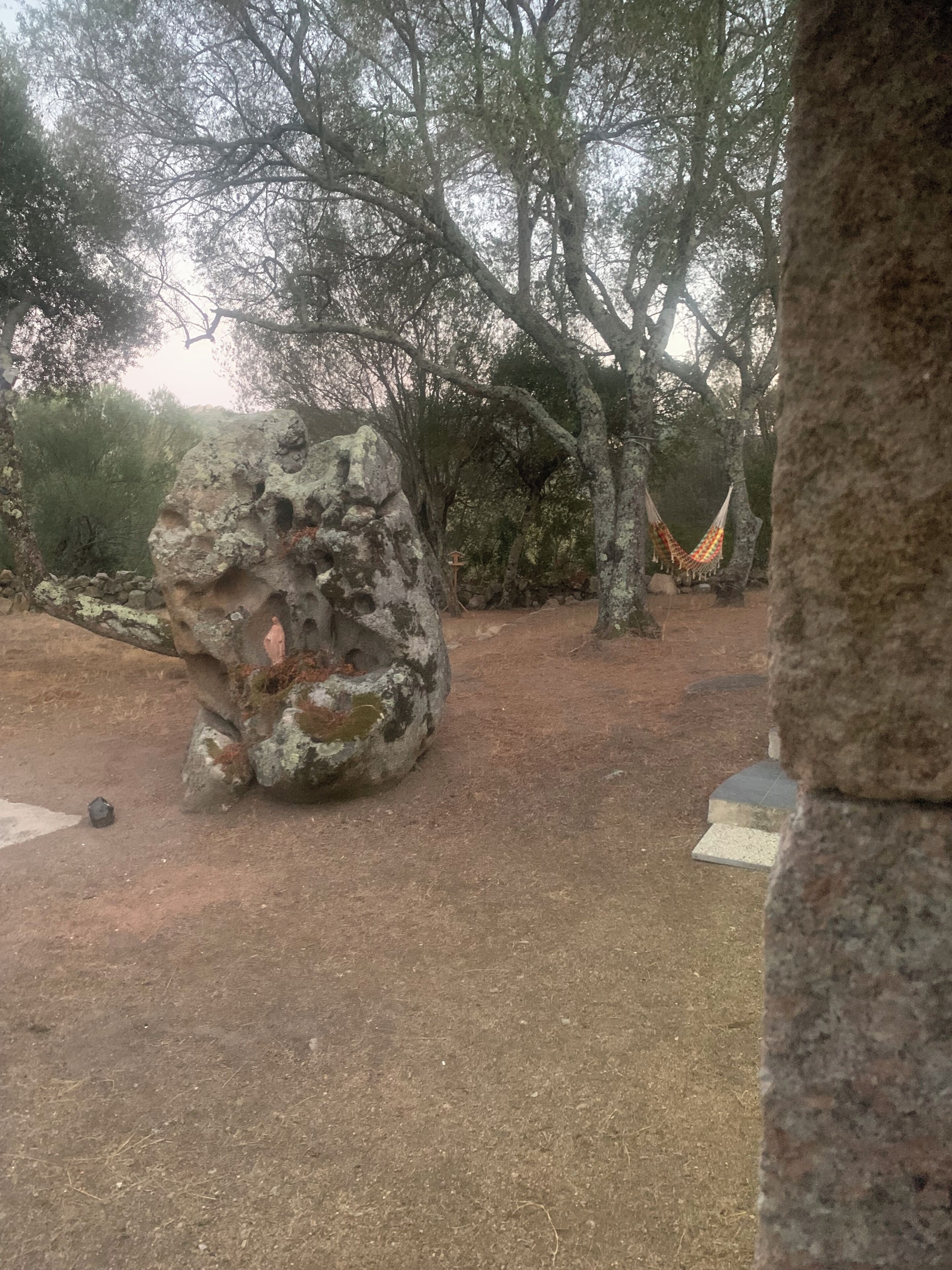 A natural outdoor area with a large rock formation, a hammock, and a stone pathway.