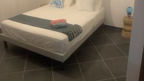 A single bed with white bedding and a blue throw blanket, a bedside table with a globe, and a wall-mounted air conditioner. - Guest room 21m2 (Figari)