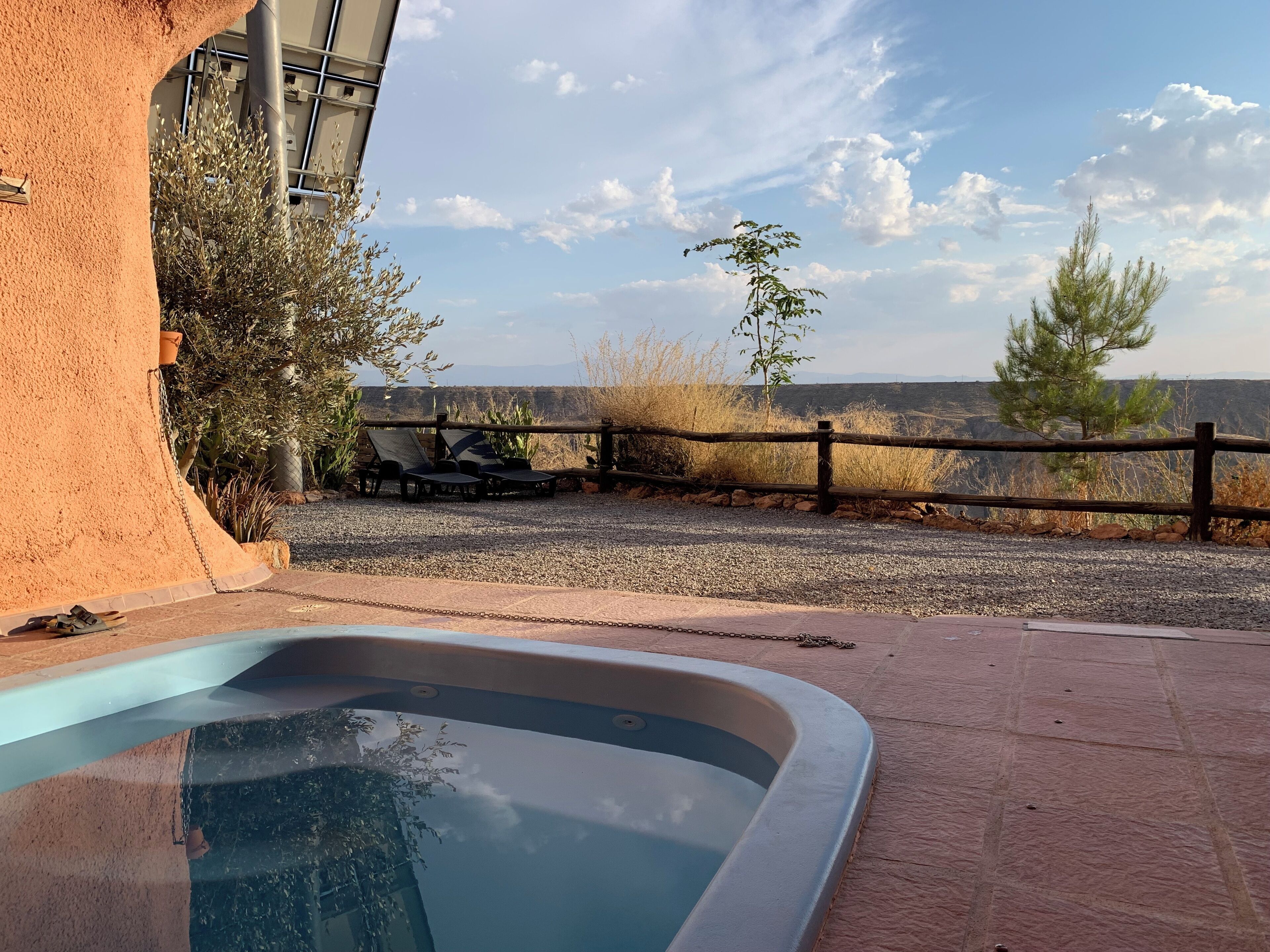 A pool area with a view of a mountainous landscape, a wooden fence, and lounge chairs.