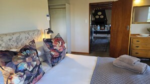 Hotellihuone, jossa on sänky, yöpöytä, lamppu, lipasto ja peili.