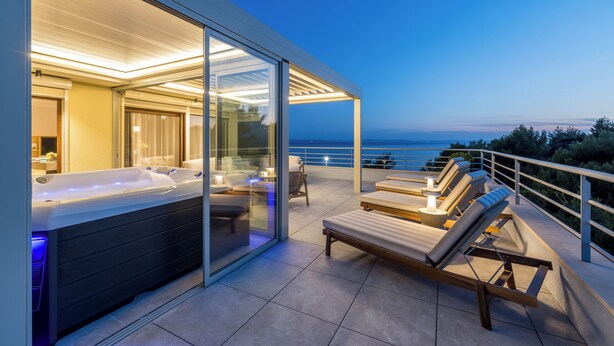 A modern outdoor hot tub area with glass doors, lounge chairs, and a view of the sea. - Beachfront Penthouse Residence (Podstrana)