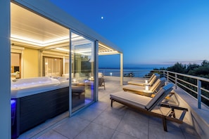 A modern outdoor hot tub area with glass doors, lounge chairs, and a view of the sea. - Beachfront Penthouse Residence (Podstrana)