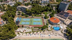 An aerial view of a coastal area with a tennis court, a swimming pool, and a beach with umbrellas and sun loungers. - Beachfront Penthouse Residence (Podstrana)