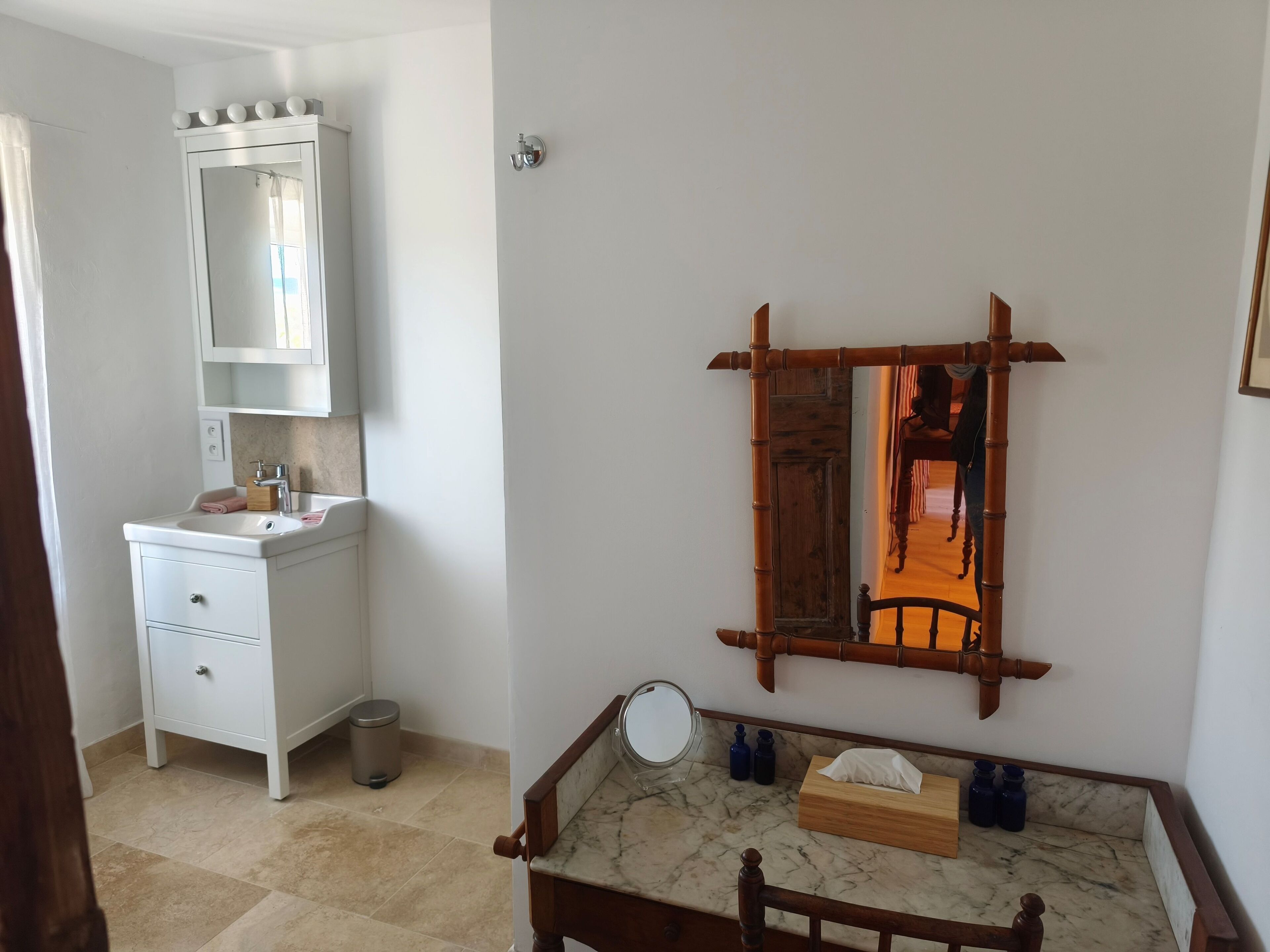 Une salle de bain avec un meuble-lavabo blanc, un miroir et une chaise en bois dotée d’un plateau en marbre.