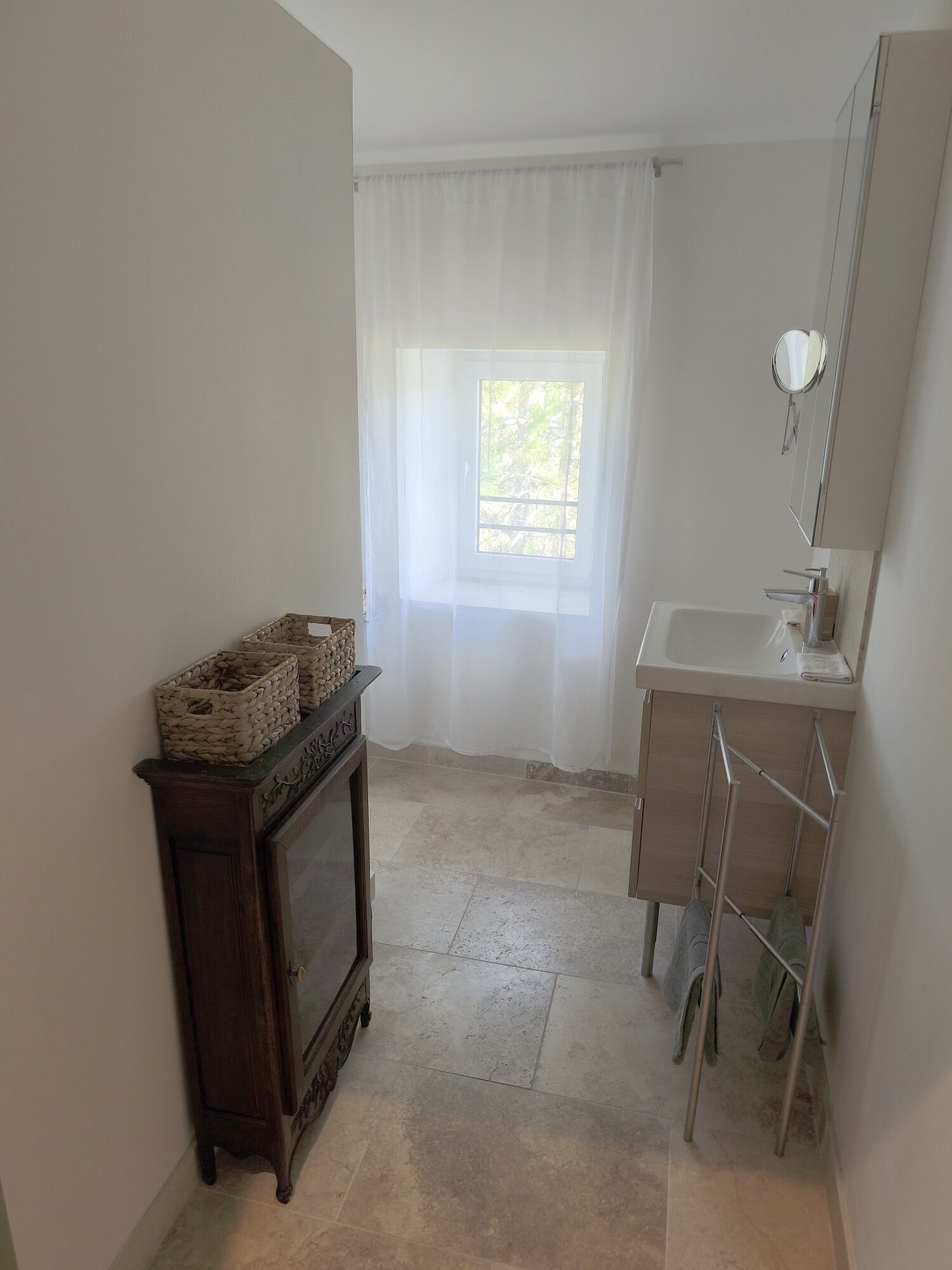 Un baño con ventana, lavabo, espejo y un mueble de madera.