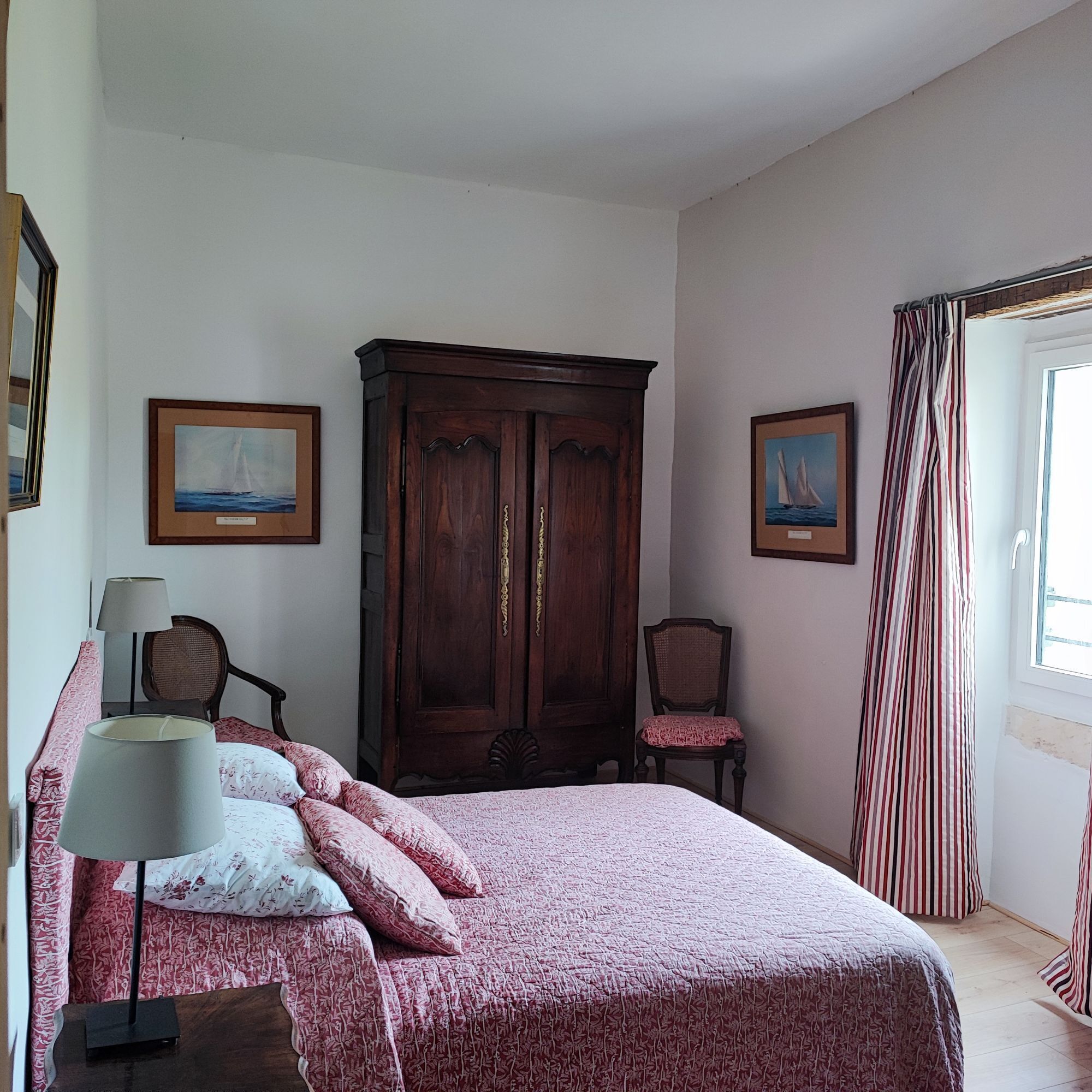 Ein Schlafzimmer mit einem Bett, einem Holzschrank, zwei Stühlen und zwei gerahmten Bildern an den Wänden.