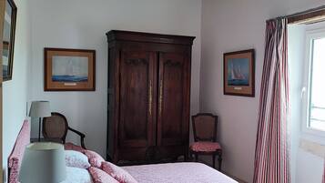 Ein Schlafzimmer mit einem Bett, einem Holzschrank, zwei Stühlen und zwei gerahmten Bildern an den Wänden.