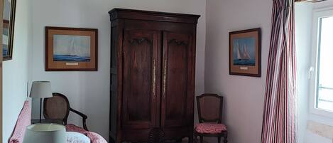 Un dormitorio con cama, un armario de madera, dos sillas y dos cuadros en las paredes.